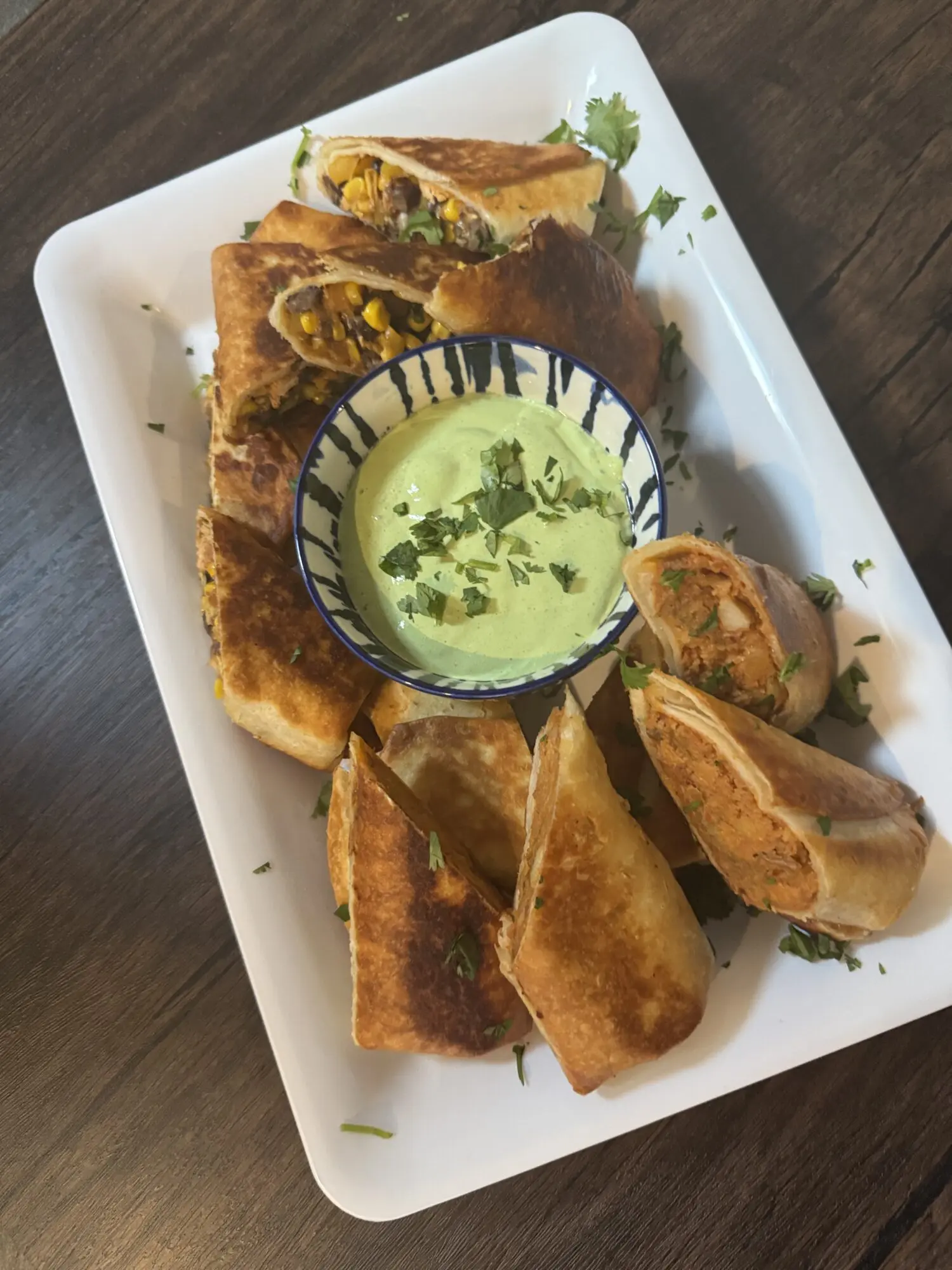 A white plate topped with food and a bowl of dip.